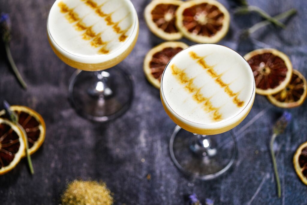 A couple of yellow cocktails from a birds-eye perspective. There are cut up slices of dried lemon around the table as decoration.