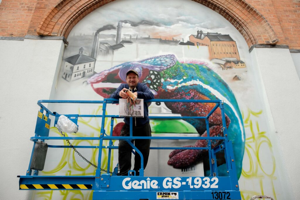 A mural artist in front of his work in Cheltenham, working as part of Cheltenham Paint Festival