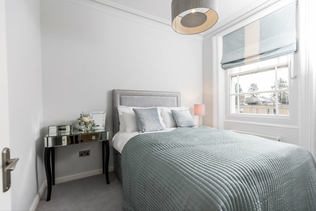 A cosy bed with a grey throw. It's in a light and airy room.